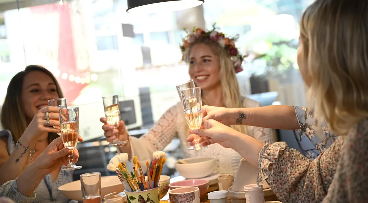 Freundinnen stoßen beim Keramikmalen mit Sekt an