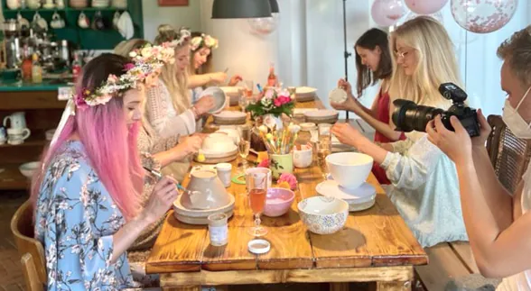 Fotograf und Gruppe mit Blumenkränzen am Maltisch